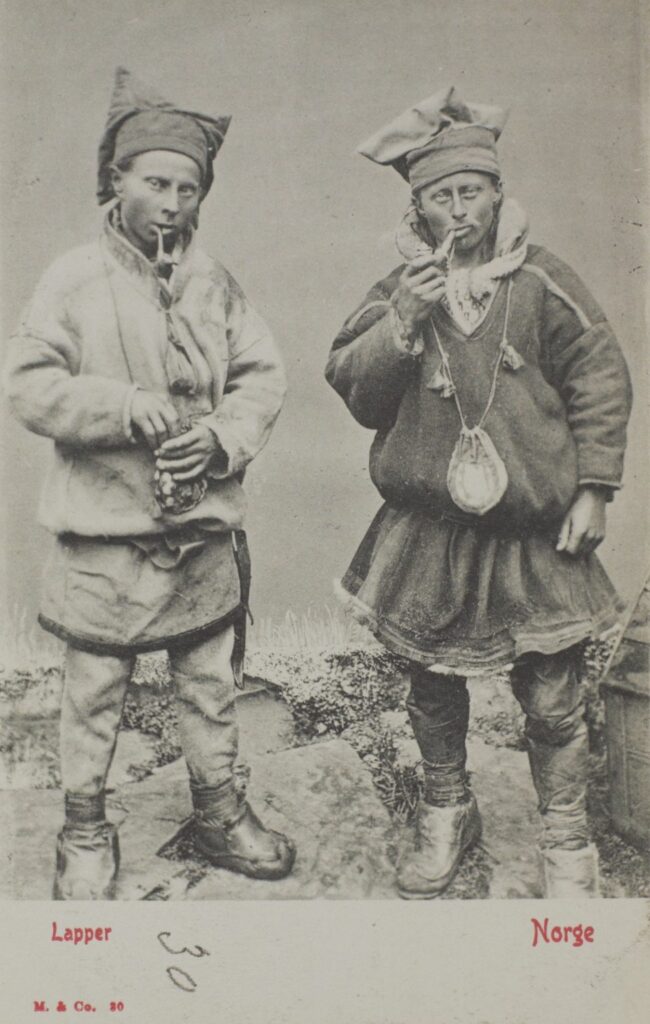 To unge samiske menn med tobakkspunger og piper. Tittel: Lapper. Norge. Postkort skapt av Mittet & Co, mellom 1900 og 1910. Universitetsbiblioteket i Bergen.